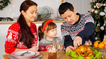 man cuts cooked fried chicken to feed family sitting at holiday table against New Year decorations closeup