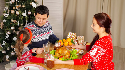 family joins hands and congratulates for Happy New Year telling wishes at festive supper near Christmas tree