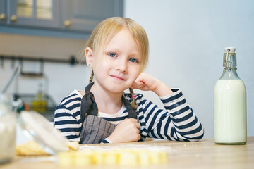 Portrait of a cute little girl in an apron preparing dough for cookies in the kitchen