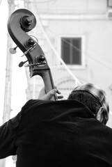 Shot from the back of a street musician playing the double bass.
