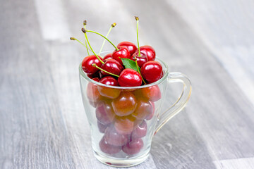 Fresh juicy red sweet cherry berries in the glass cup on light wooden background in summer.