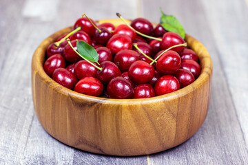 Fresh juicy red sweet cherry berries in the wooden bowl on light background in summer.