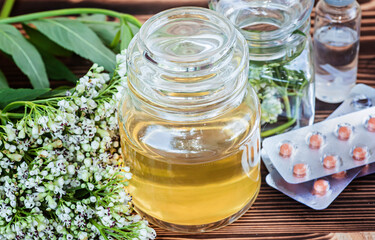 Fresh Valeriana officinalis flowers in transparent jar. Valerian tablets among white flowers are on...