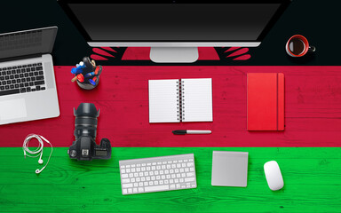 Malawi flag background with headphone,camera, notebook and mouse on national office desk table.Top view with copy space.Flat Lay.