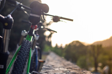 Closeup of mountain bikes standing leaned on a wall. Multiple bikes, later afternoon sunset golden hour. Friends resting their bikes doing extreme sports