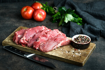 Fresh beef steaks on a board on a dark background with spices and herbs.