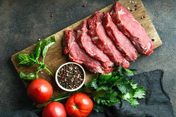 Fresh meat on a cutting board with ingredients for the preparation. Cut pork on a dark background top view with copy space.