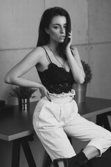 Woman in white trousers and black top sitting at table in simple loft interior