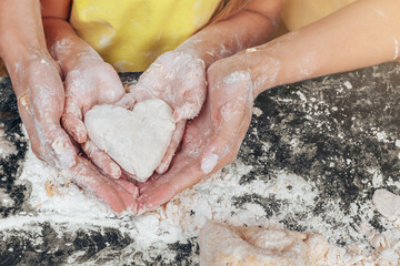 Mom and daughter are holding a heart made of dough. Cook in the kitchen on a black table close-up