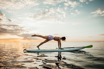 Young woman doing YOGA on a SUP board in the lake at sunrise