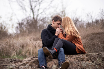 Beautiful guy and girl sit on a big stone and cuddle, love, romance, it warms her cold evenings