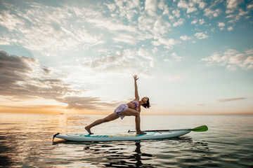 Young woman doing YOGA on a SUP board in the lake at sunrise - Powered by Adobe