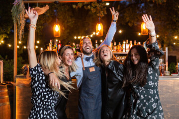 group of girls with boy (bartender) hugging, celebrating and dancing in front of the bar outside. night pub. club.