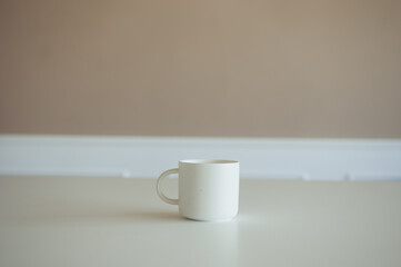 Empty white cup on beige background, space for text