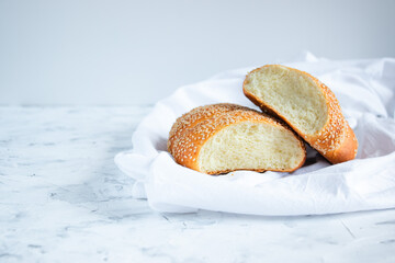 Sliced rolls sprinkled with sesame seeds on a white towel. Home baking and breakfast concept. Copy space for your text.