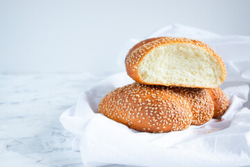 Sliced bun with sesame seeds on a white towel, copy space for your text. Home baking and breakfast concept.