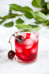 Cherry fruit drink in a glass cup, cherry berries and green leaves on a white background. A refreshing summer drink.