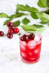 Cherry fruit drink in a glass cup, cherry berries and green leaves on a white background. A refreshing fruit summer drink.