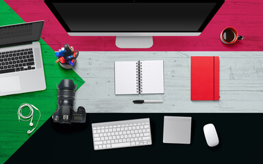 Sudan flag background with headphone,camera, notebook and mouse on national office desk table.Top view with copy space.Flat Lay.