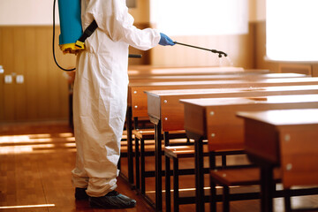 Man wearing protective suit disinfecting school class with spray chemicals to preventing the spread...