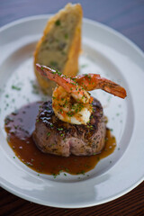 Surf ‘n Turf, lobster tail and steak entree. Filet mignon topped with chanterelle mushrooms & Maine lobster tail topped w/ drawn butter served on white dinner plate. Classic steakhouse menu favorite.