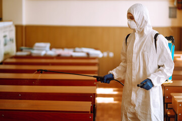 Disinfecting school class to prevent COVID-19. Man in protective hazmat suit with spray chemicals to preventing the spread of coronavirus, pandemic in quarantine city. 
