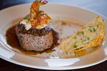 Surf ‘n Turf, lobster tail and steak entree. Filet mignon topped with chanterelle mushrooms & Maine lobster tail topped w/ drawn butter served on white dinner plate. Classic steakhouse menu favorite.