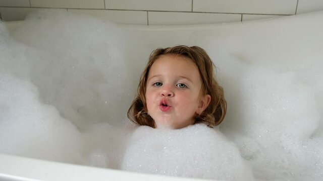 Adorable bath baby girl sings in the foam bathtub