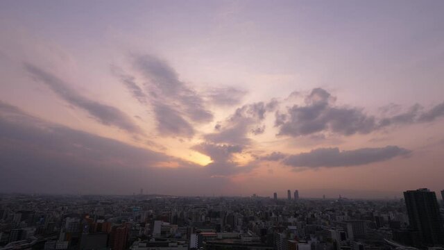 Neat colours of evening sky over Osaka city, view from high point. Dark cityscape, yellow glow seen after grey-blue clouds, sun falling down. Wide angle aerial shot