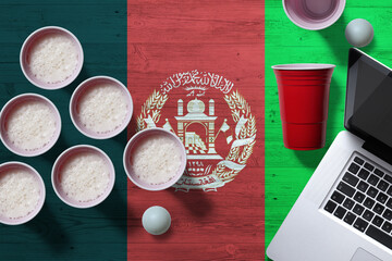 Afghanistan flag concept with plastic beer pong cups and laptop on national wooden table, top view....