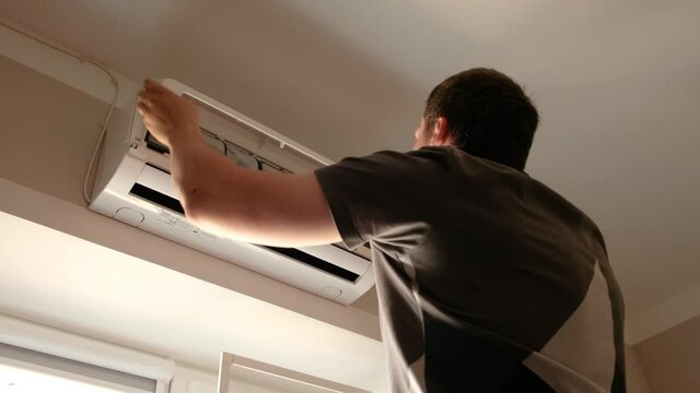 Man cleaning the air conditioner filters. He opens the lid of the air conditioner and sees very dirty filters in the dust. Air conditioning service