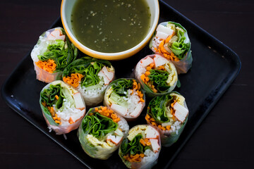 Portion of spring rolls on old wood with spicy sauce, vegetables and in noodle tube