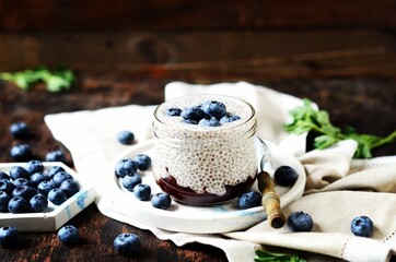 Chia pudding with jam and blueberries in glass jars on a dark wooden background, still life