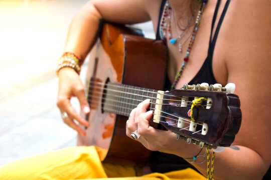 Close up of beautiful hippie woman hand with multi-colored stone bracelets playing guitar on the square outdoors. Sunlight on the photo. Music and free lifestyle