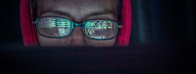 hacker at computer data reflecting in eyeglasses