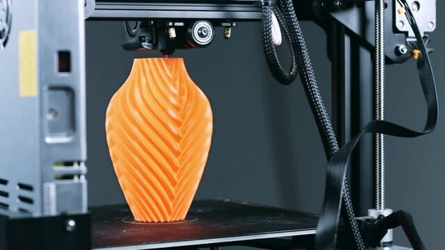 3D Printer printing a vase for home decoration with orange plastic Filament.