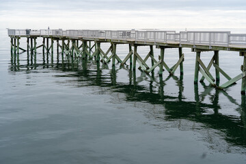 Obraz premium A view of the long pier and the Long Island Sound at Calf Pasture Beach in Norwalk, Connecticut USA on a cold and grey December day. The flat light lends a dreamy feel to the scene.