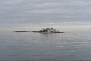 A view from the pier across the Long Island Sound to a small island off Calf Pasture Beach in Norwalk, Connecticut USA on a cold and grey December day. The flat light lends a dreamy feel to the scene.