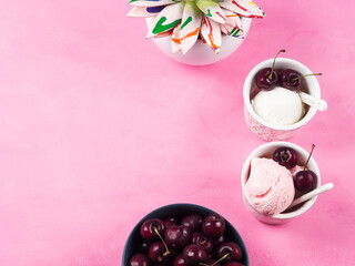 Obraz na płótnie Canvas Two cups with frozen yogurt ice cream scoops with cherries on pink background. Top view with colorful succulent plant and bowl of berries
