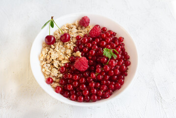 Healthy breakfast of granola and fresh berries of red currant, cherry and raspberry in a white bowl