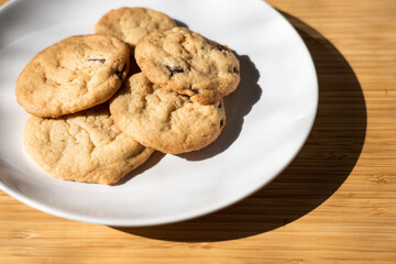A pile of delicious chocolate chip cookies arranged on a white plate on a butcher block wooden slab
