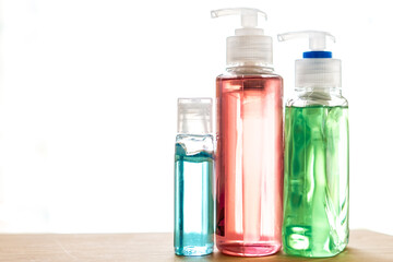 Obraz na płótnie Canvas Brightly colored green, pink and blue bottles of hand sanitizer and anti-bacterial hand gel on a wooden counter, white background