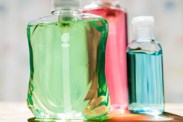 Brightly colored green, pink and blue bottles of hand sanitizer and anti-bacterial hand gel on a wooden counter