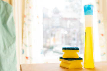 Cleaning products: A tall yellow bottle of anti-bacterial spray and two yellow sponges
