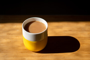 A lovely cup of tea in a bright yellow and white mug; on a butcher block slab in bright morning sun...