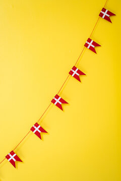 A string of little wooden Danish flags (Dannebrog) against a bright yellow background.