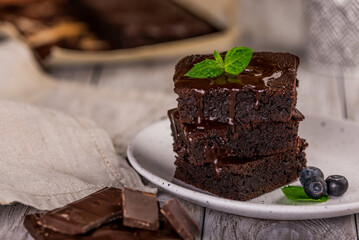 A stack of chocolate brownies on wooden background with mint leaf on top, homemade bakery and...