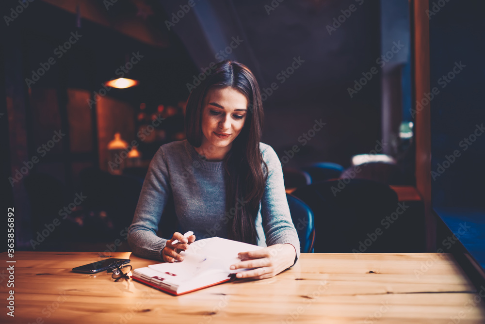 Poster young businesswoman browsing pages of own diary notepad and searching useful information while sitti