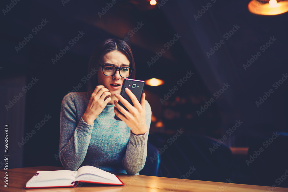 Aufkleber hipster girl in eyeglasses worrying and watching online broadcasting on mobile phone while preparing
