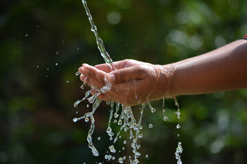 Naklejka na ściany i meble Water Pouring In Kid Two Hand On Nature Background. Hands With Water Splash.